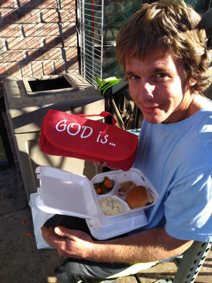 A person receiving a meal with a package that says, "God is..."