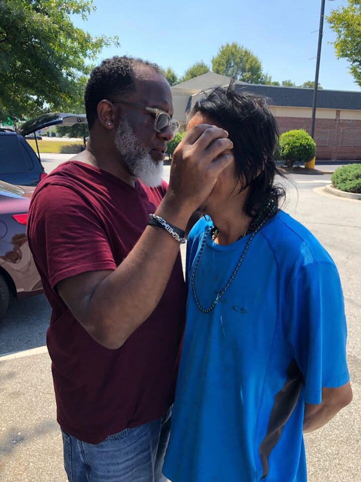 Will Francis of Lives and Souls Missional Church praying over an invididual in a parking lot.